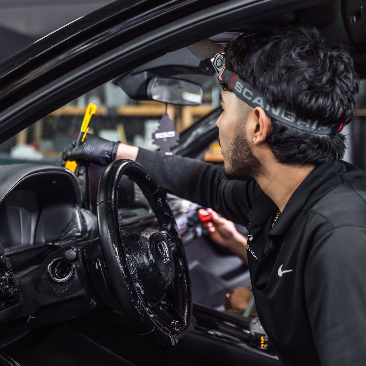 Person cleaning a car dashboard, wearing black gloves and a headlamp.