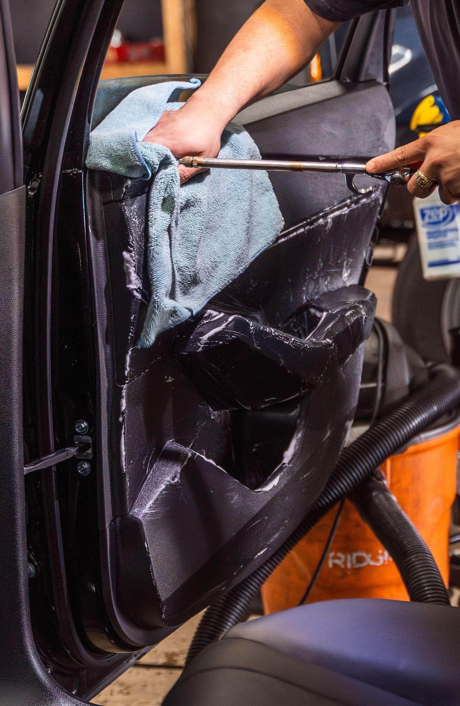 Person installing window tint on a car door, using a tool and cloth to apply.