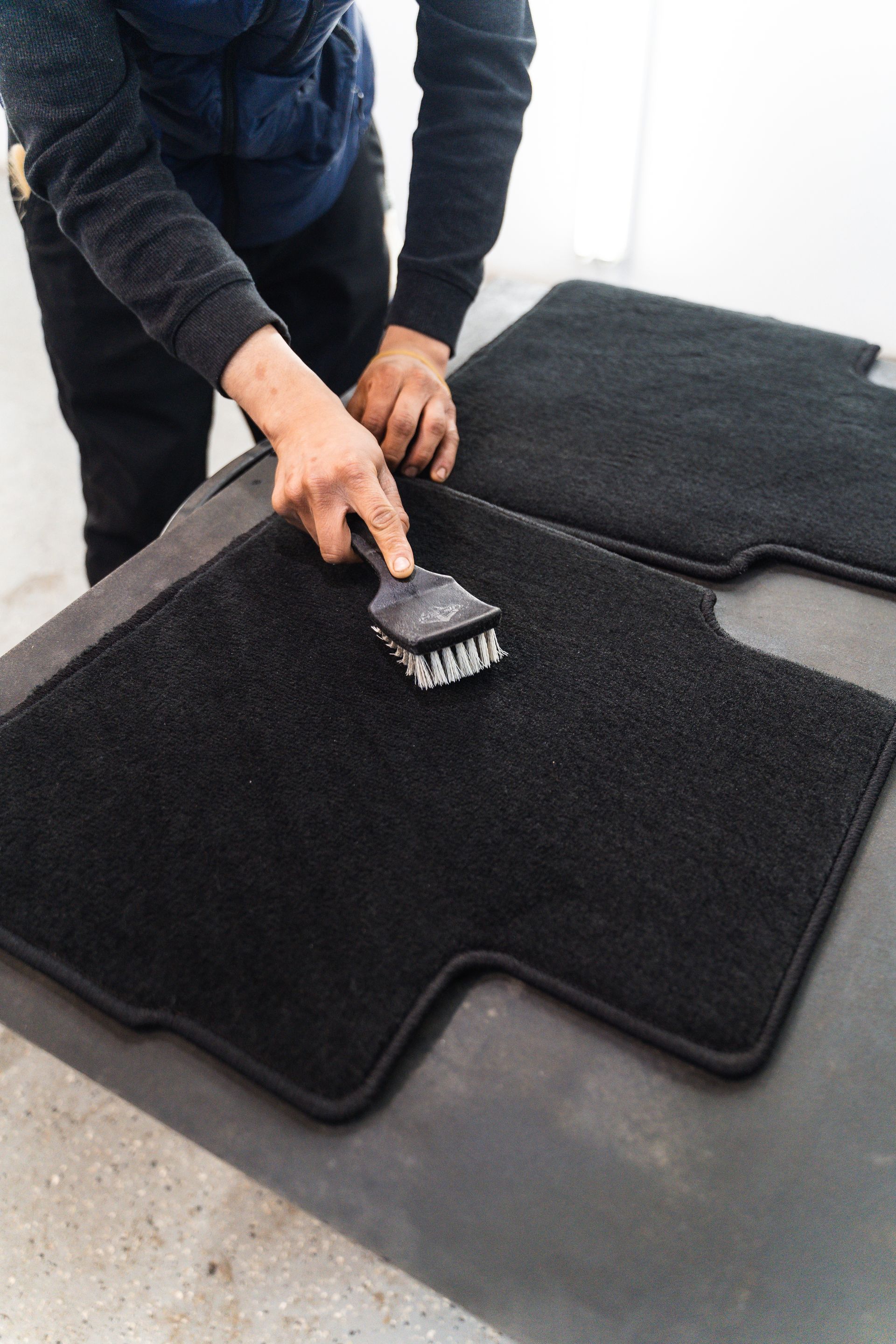 Hand scrubbing the inside of a car trunk with a brush, removing dirt from grooves.
