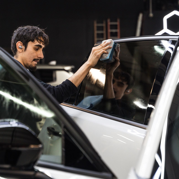 Person cleaning car window with a sponge in a garage, reflected in the glass.