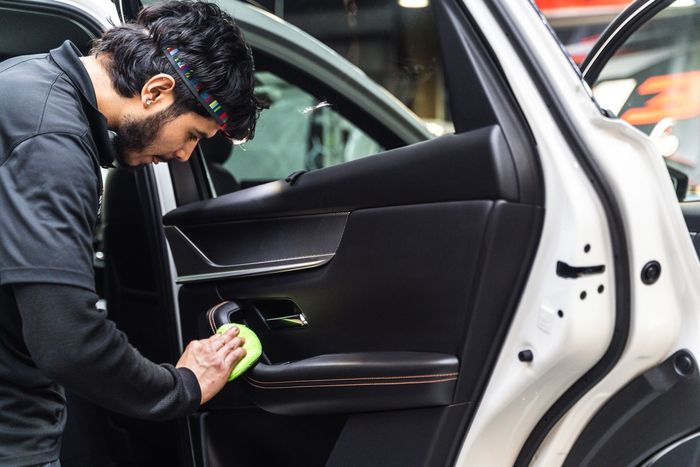Man cleaning a car door's interior with a green cloth. He wears a headlamp and a dark shirt inside a garage.