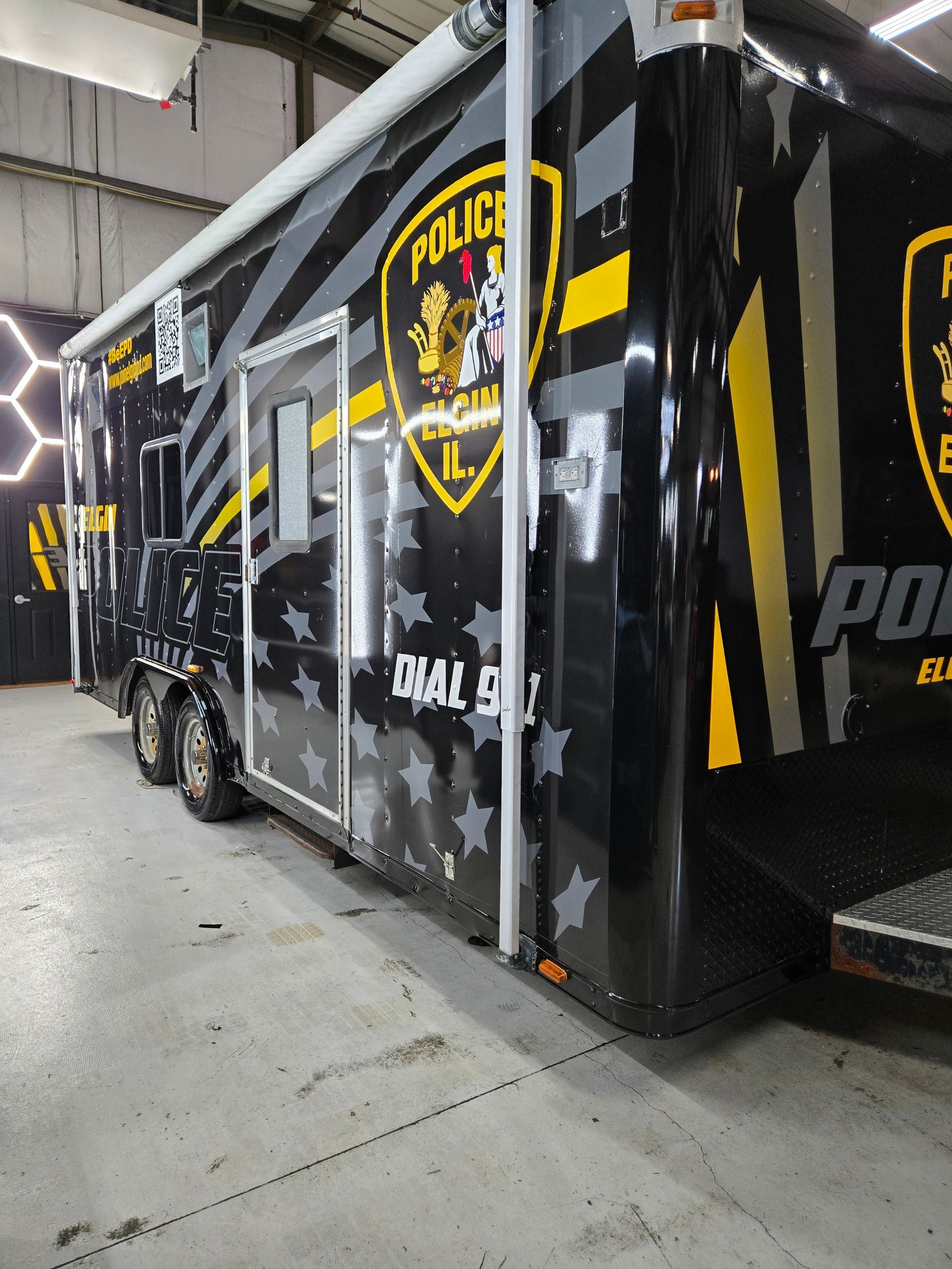 Black police mobile command unit with yellow accents and a star pattern, parked indoors.