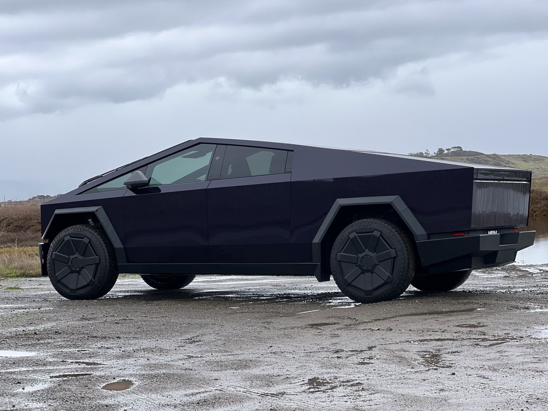 A black tesla cybertruck is parked in a dirt field.