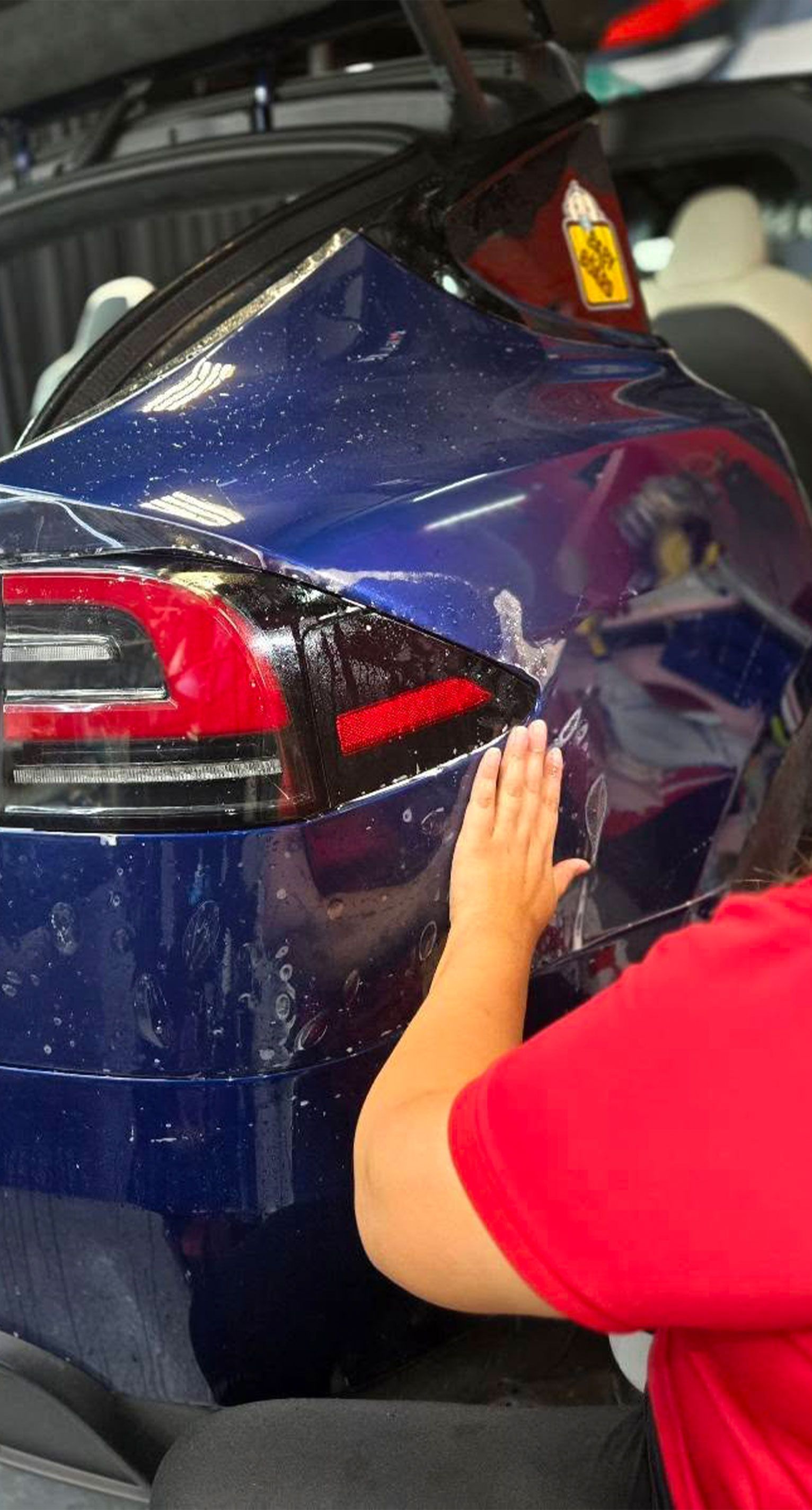 Person's hand smoothing blue film on a car's rear, near a red taillight.