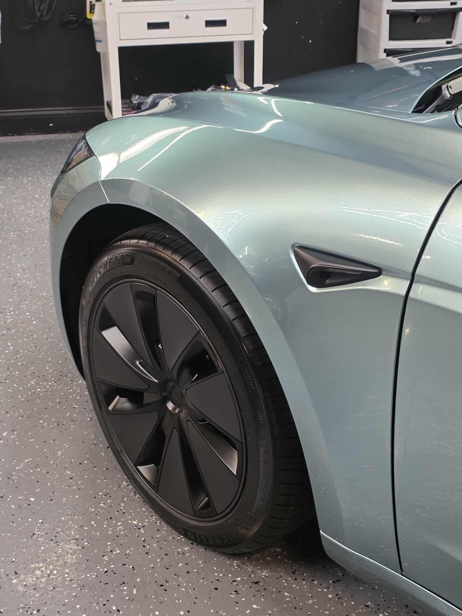 Light blue Tesla car front quarter with black wheel. Indoors, shop setting.