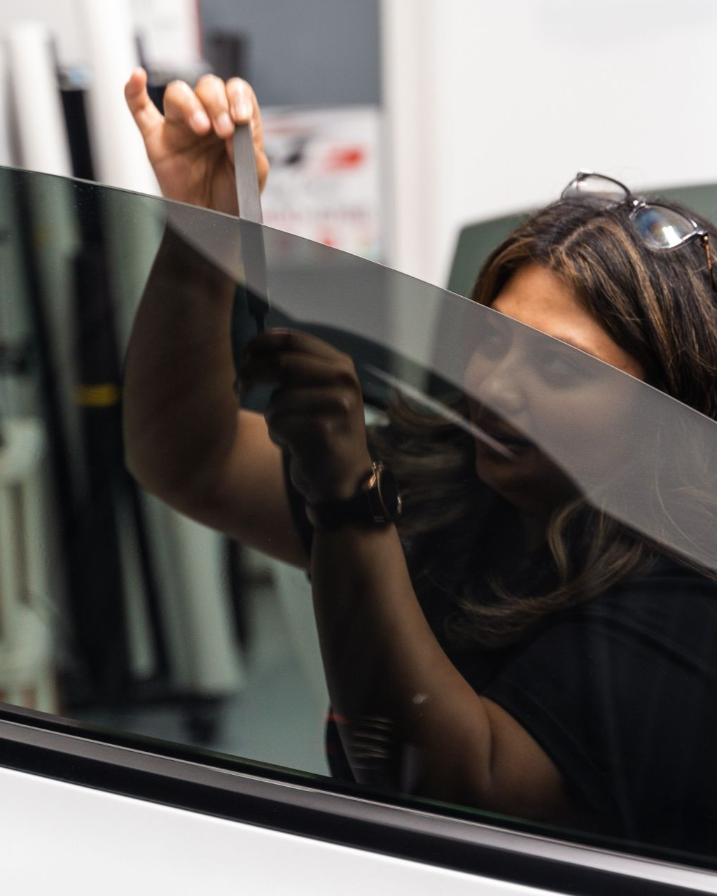 White car side, tinted windows, chrome door handle and window trim, reflecting overhead lights.