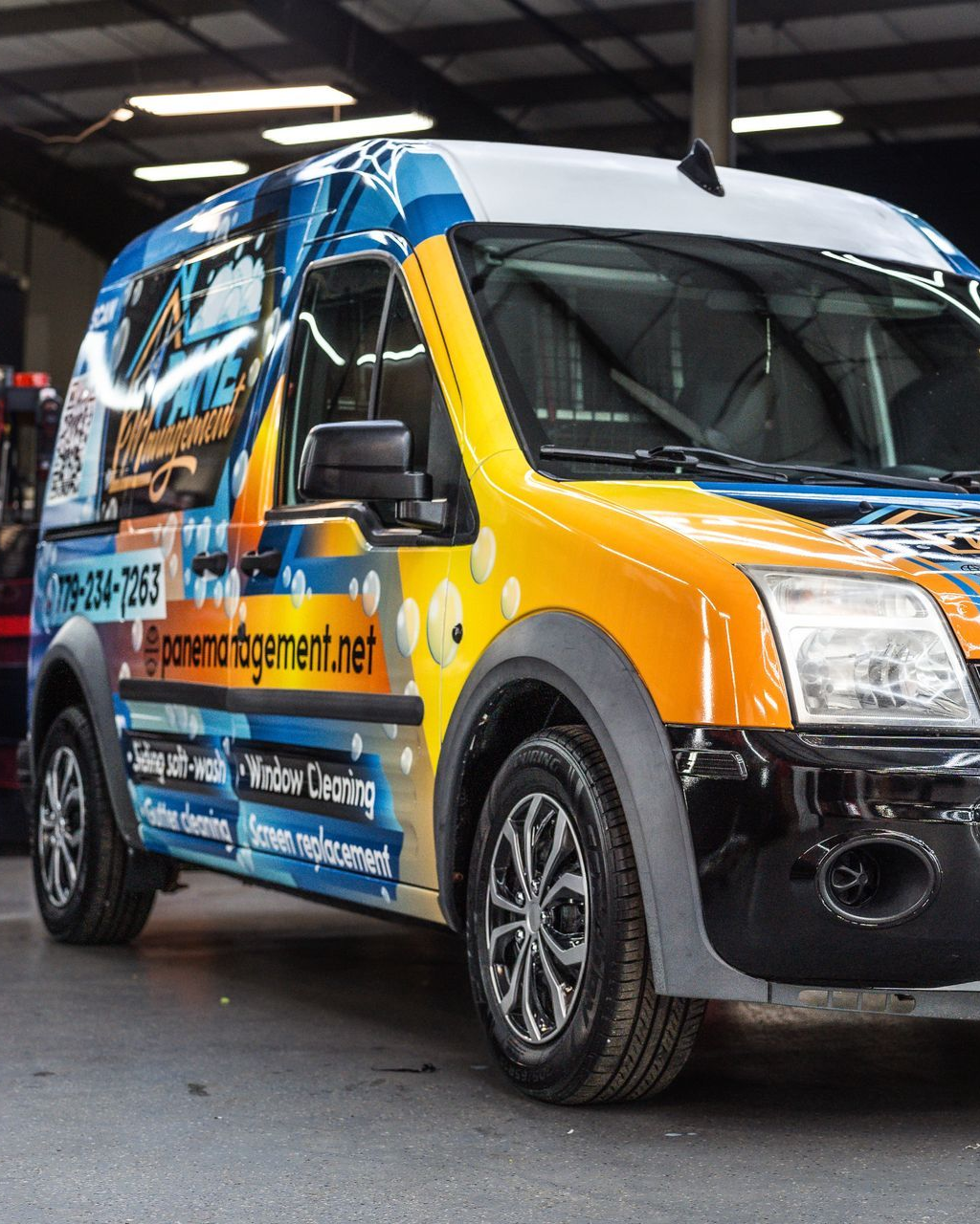 A yellow and blue commercial van featuring a custom wrap with graphics and text, parked inside a garage.