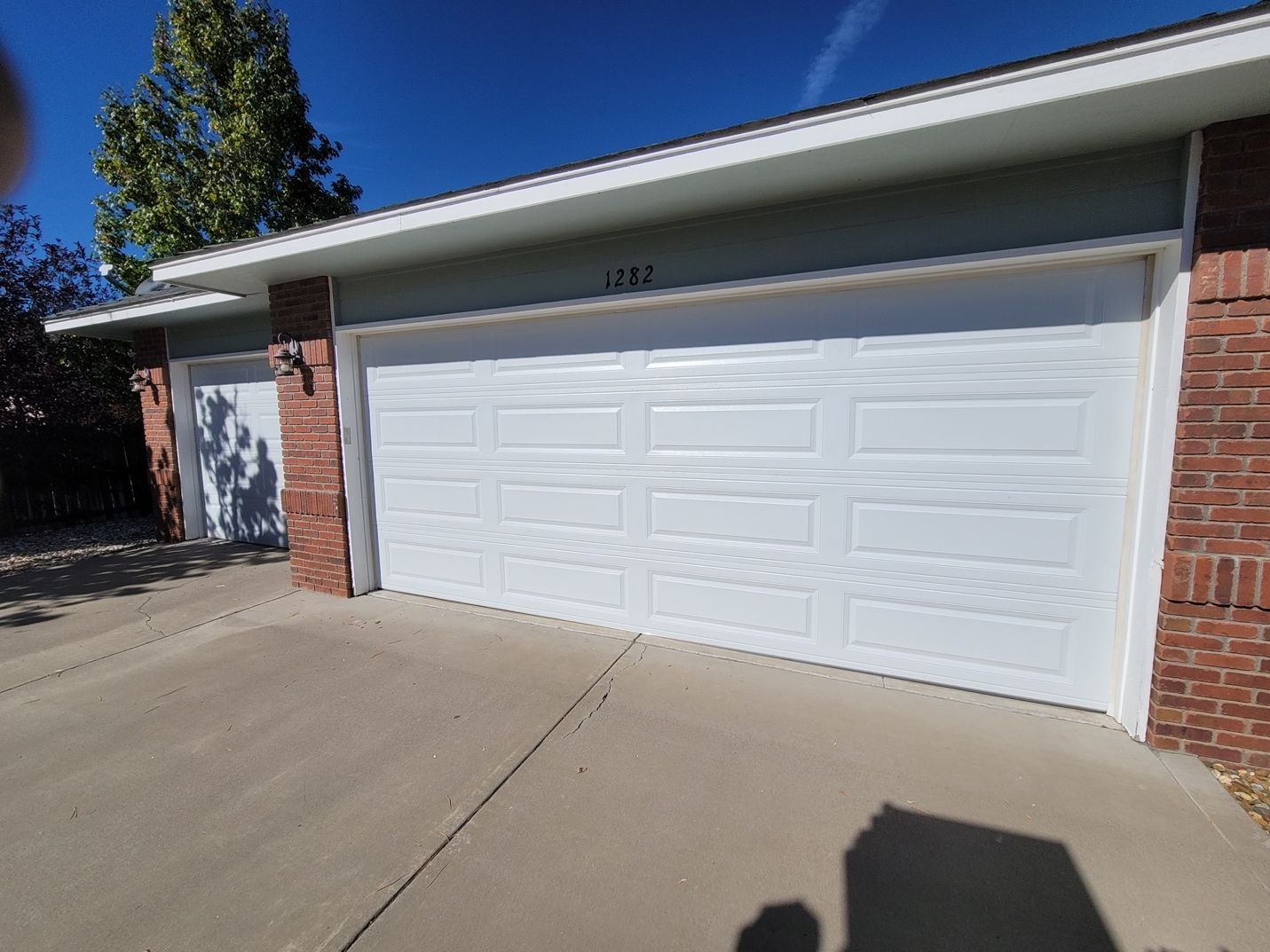 A white garage door is sitting next to a brick building.