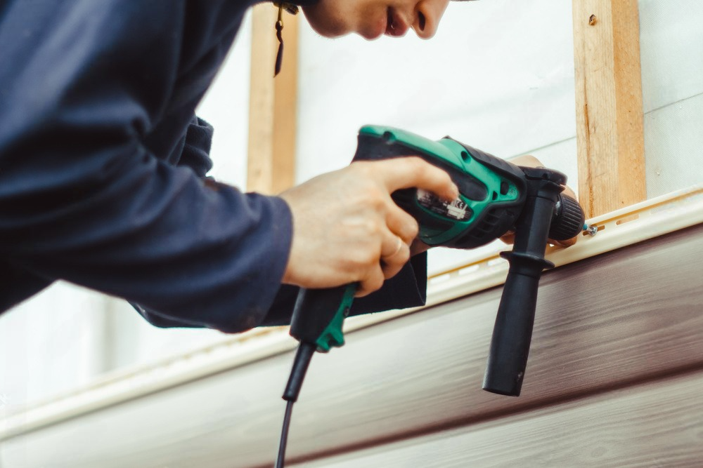 a man is using a green and black drill on a siding of a house