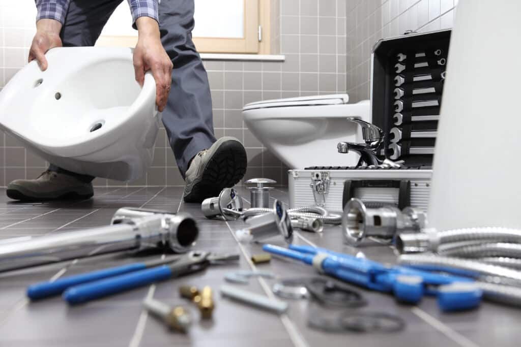 Plumber in blue hard hat and gloves using wrench on pipes in a utility room.