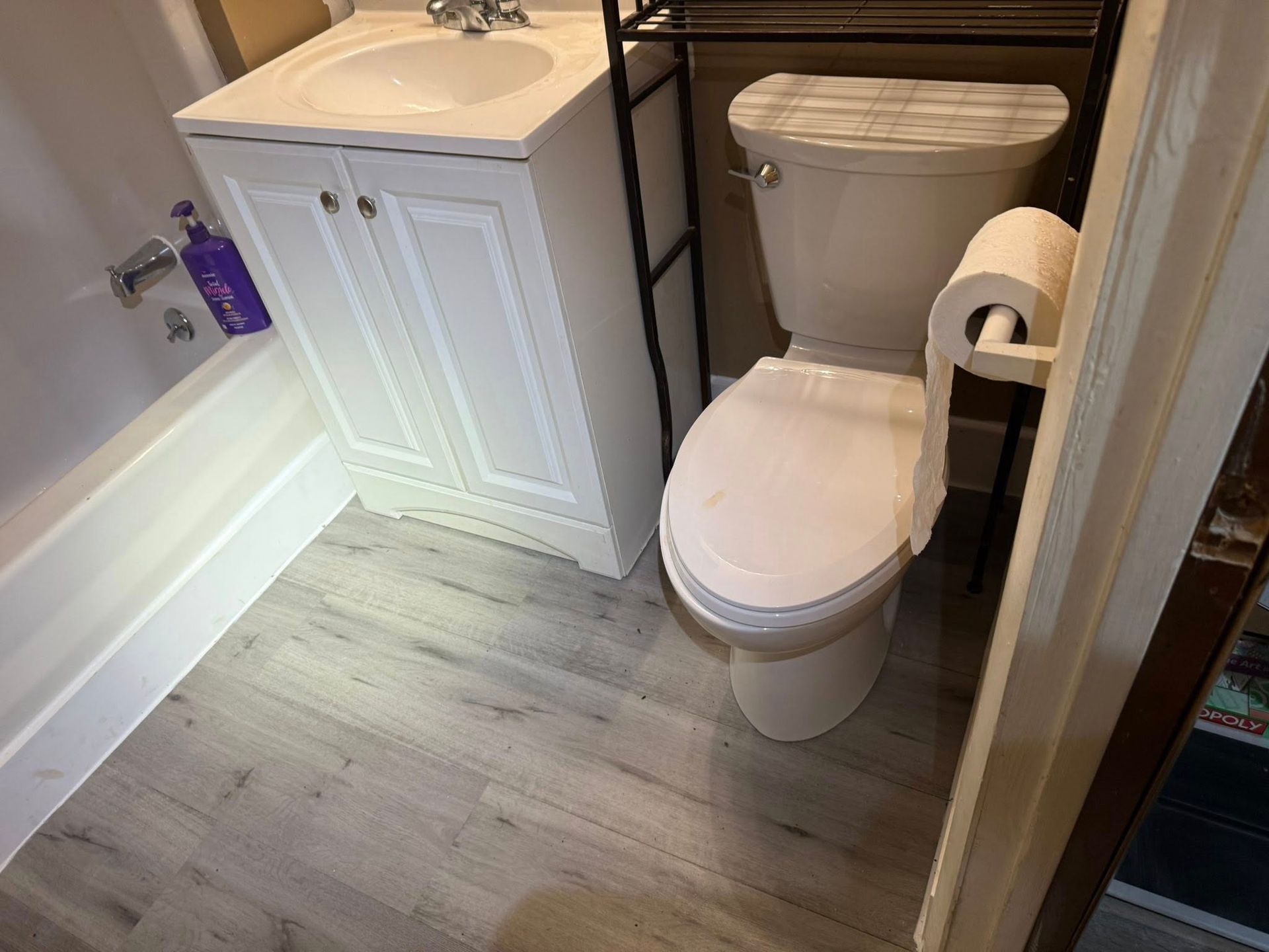 Bathroom with a toilet, sink, and bathtub. Light gray flooring and off-white cabinets.