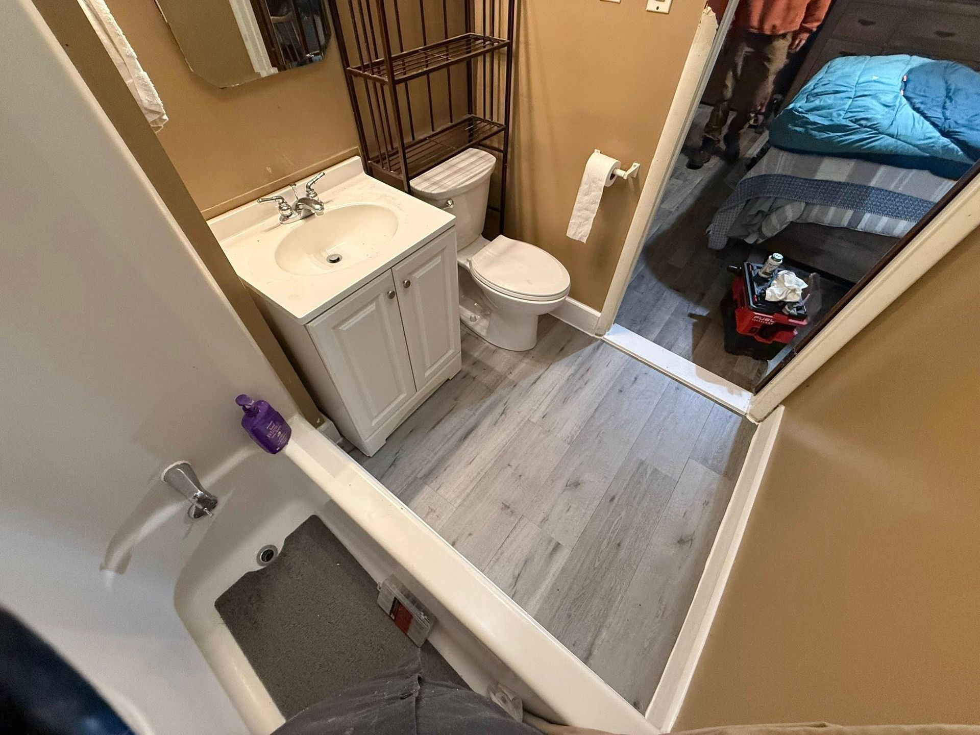 Bathroom with white vanity, toilet, and shower. The doorway leads to a bedroom.