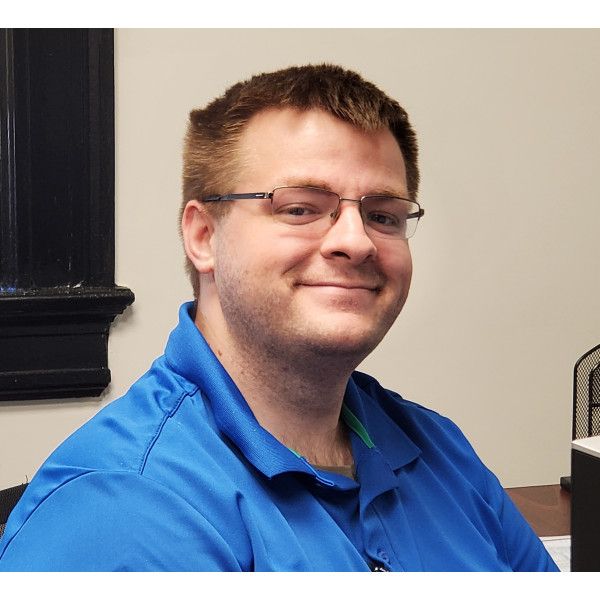 A man wearing glasses and a blue shirt is smiling for the camera