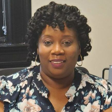 A woman in a floral shirt sits at a desk