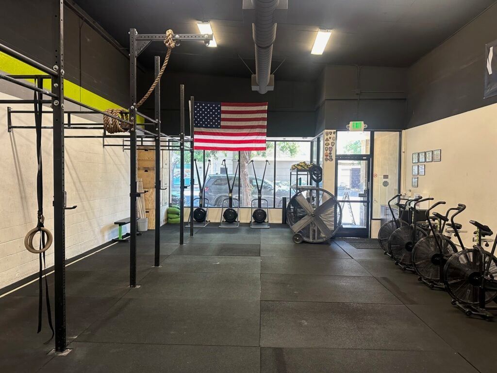 Interior of a gym with exercise equipment. Features include pull-up bars, weights, bikes, and an American flag.