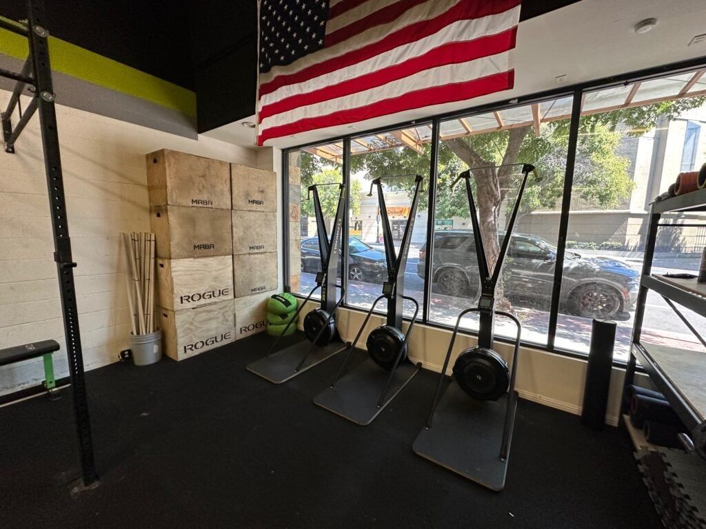 Gym interior with three air bikes, boxes, an American flag, and a pull-up bar.