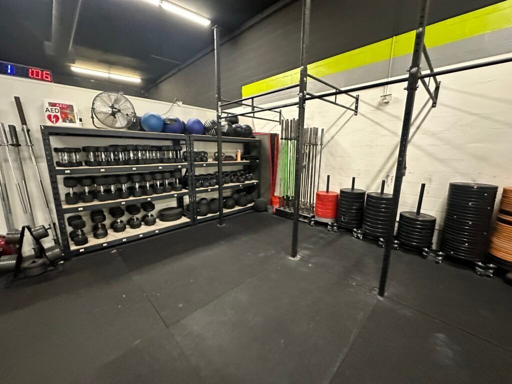 Interior of a gym with weights, pull-up bars, and exercise equipment. Black floor and shelves, brightly lit.