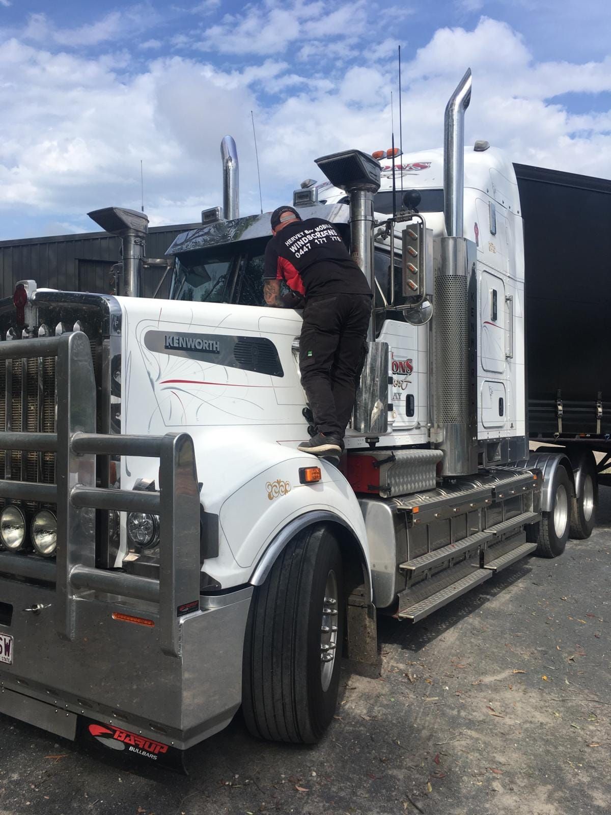 A person is standing on the front of a white semi-truck, working on the vehicle. — Hervey Bay Mobile Windscreens in Pialba, QLD