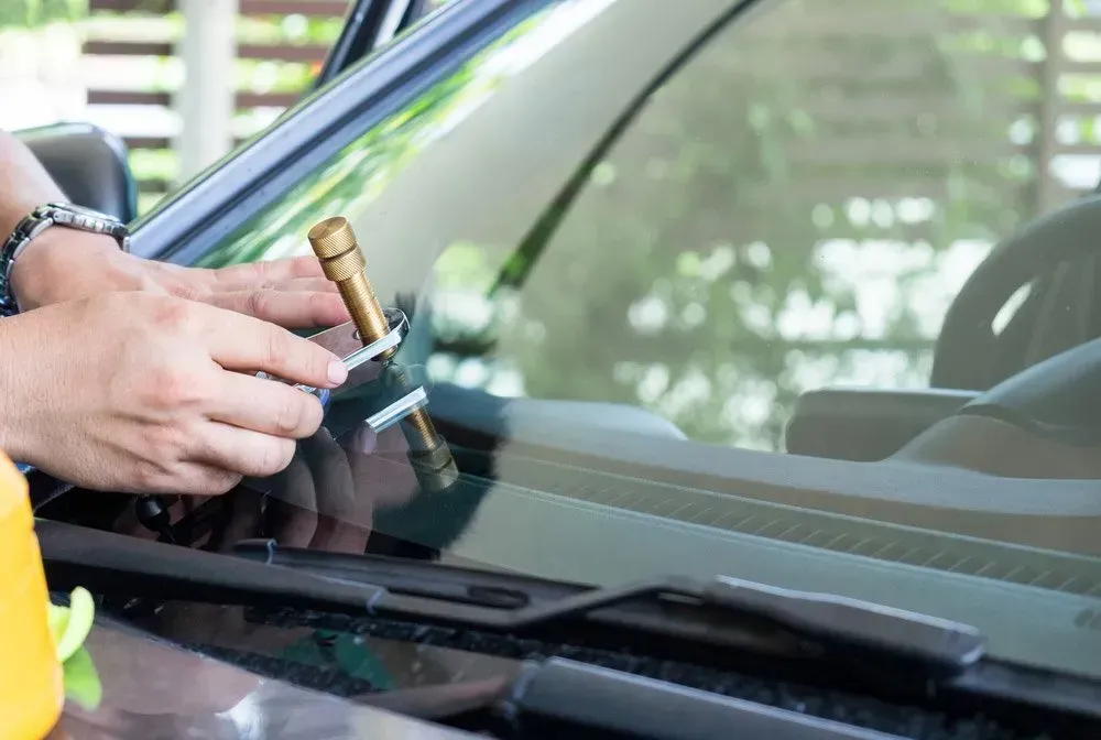 Person Repairing a Cracked Car Windshield with A Tool Outdoors — Hervey Bay Mobile Windscreens in Pialba, QLD