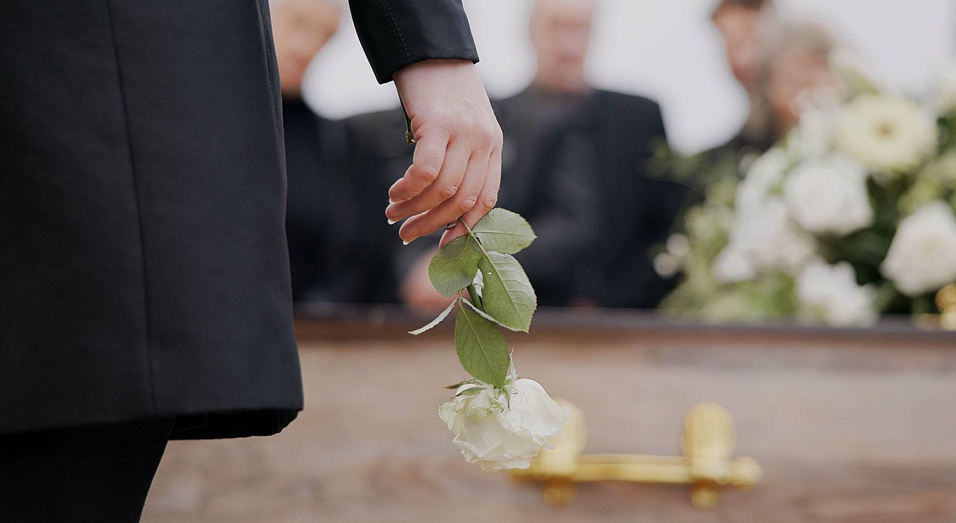 A person is holding a flower in front of a coffin at a funeral.