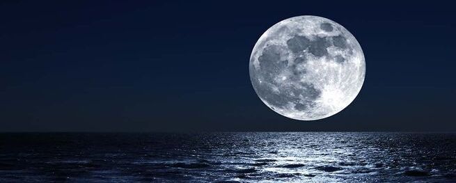 's Nachts komt er een volle maan op boven de oceaan.