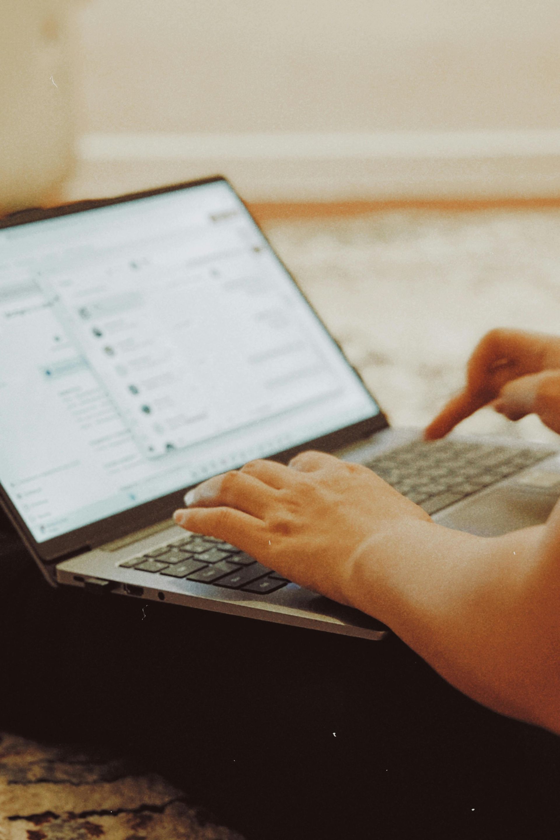 Person using a laptop, typing with both hands, seated on a patterned rug.
