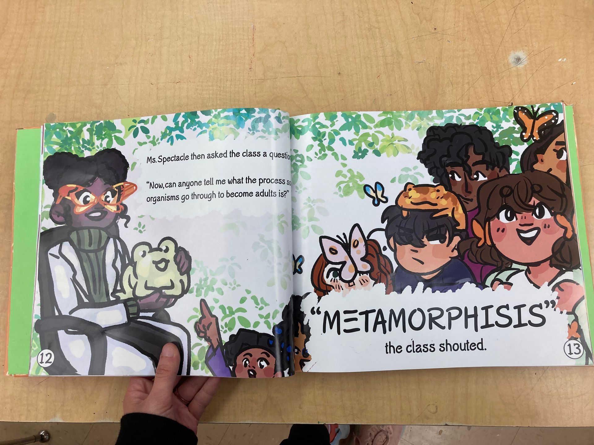 Person holds open book: illustrated pages about metamorphosis with cartoon children and frog.