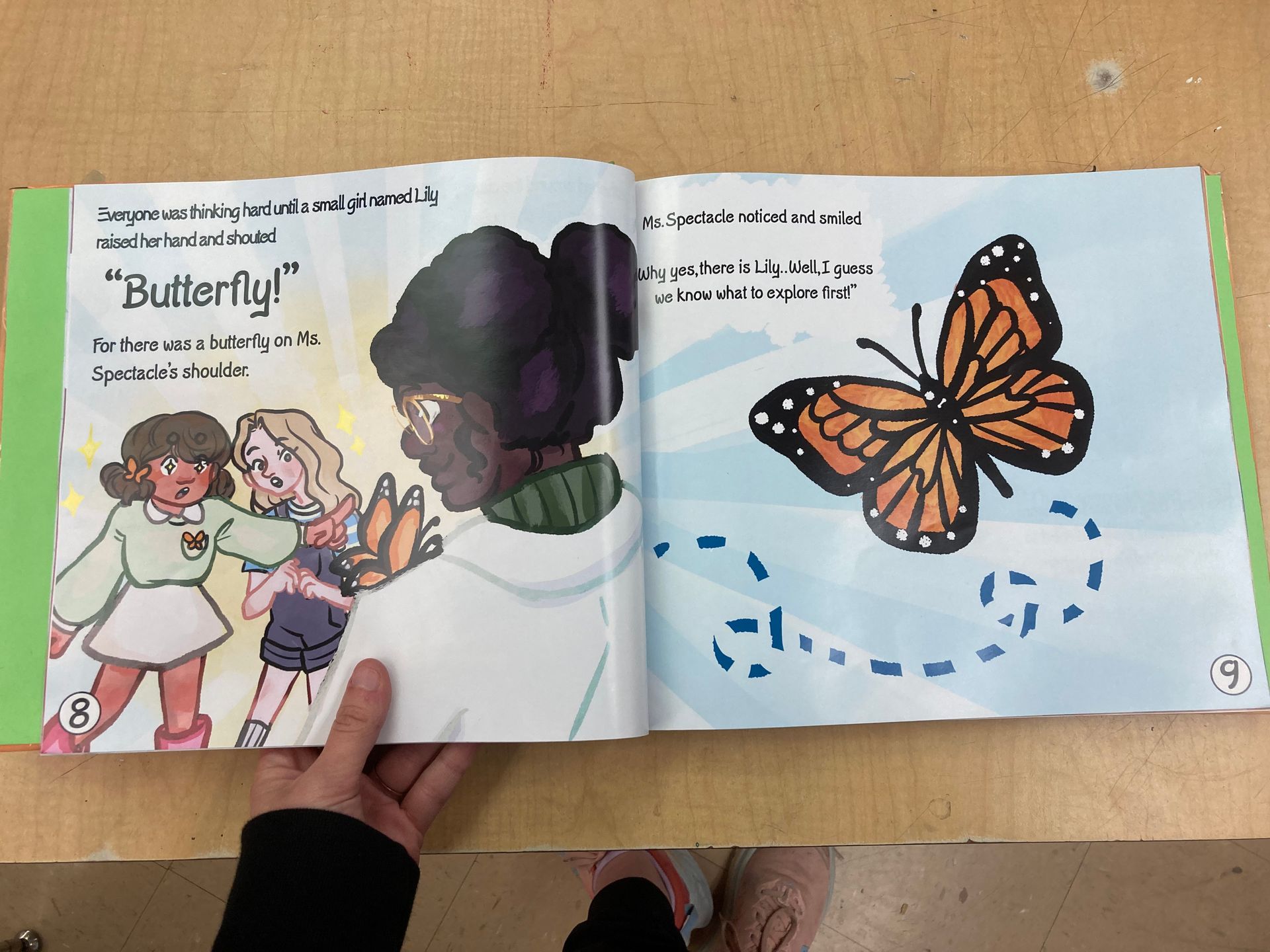 Open book with illustrations. Three children react to a butterfly. The butterfly is orange and black.
