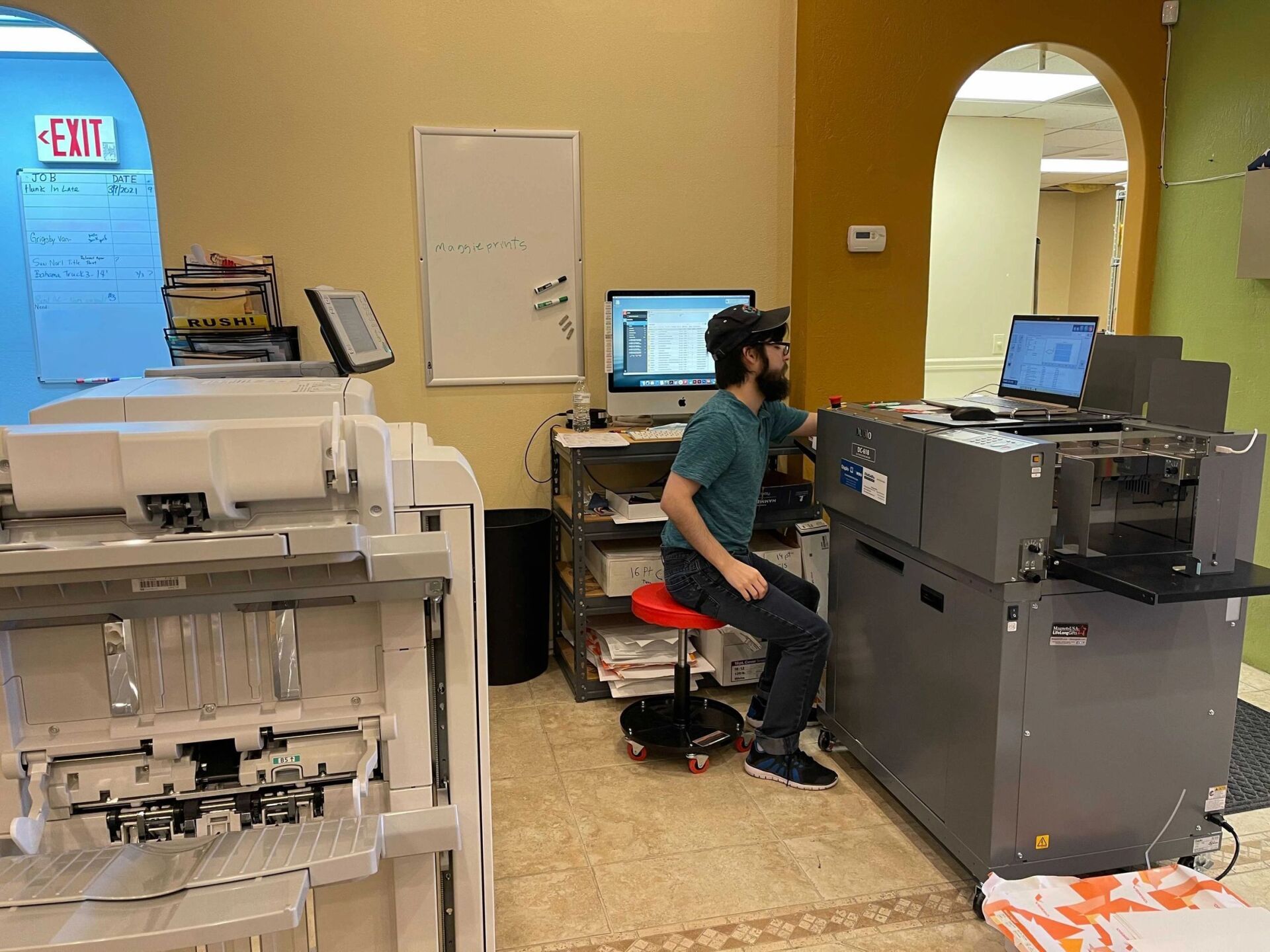 A person works on printing equipment in an office. They're seated, operating the machine.