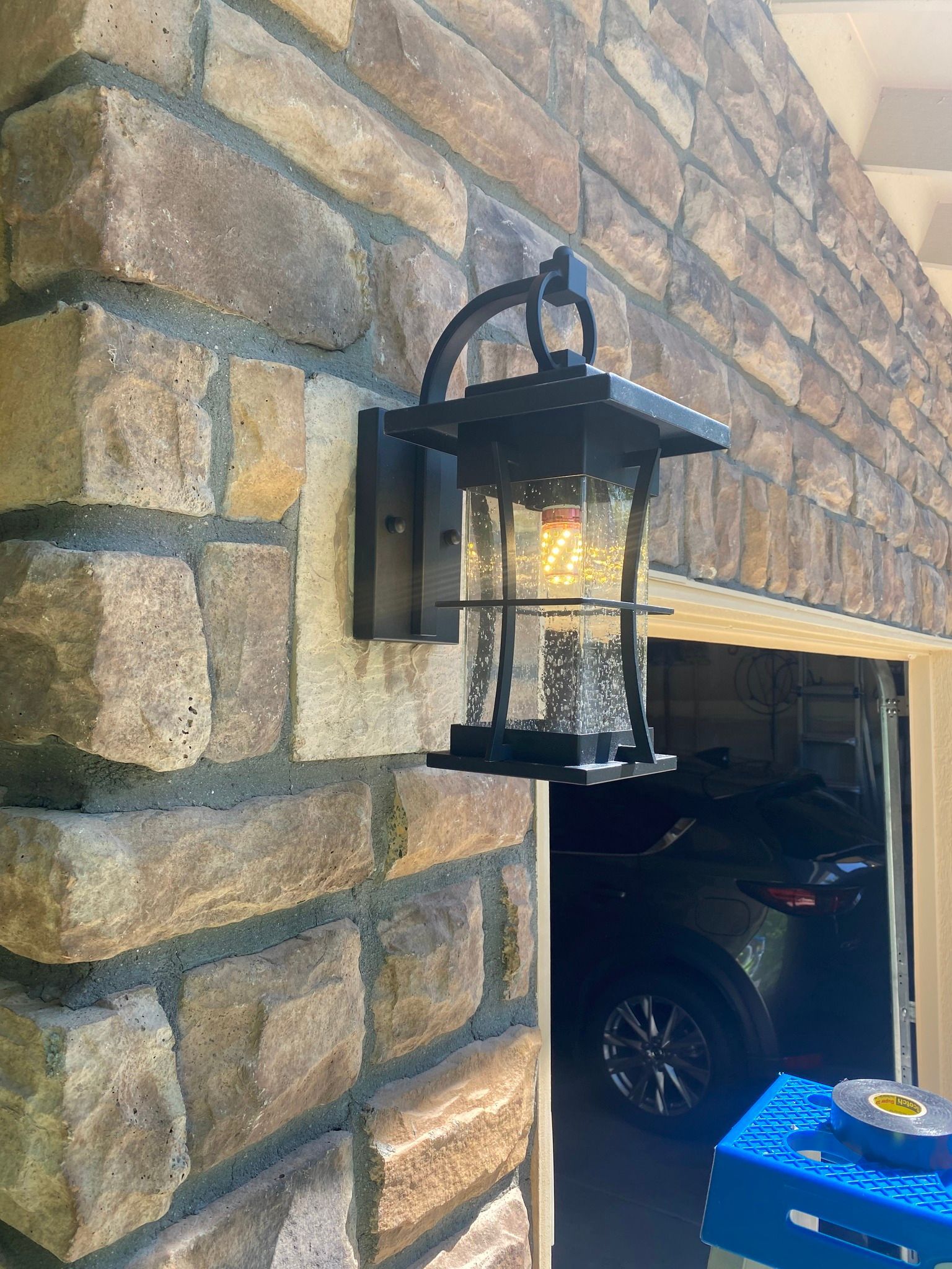 Black outdoor light fixture on a brick wall, near a garage entrance.