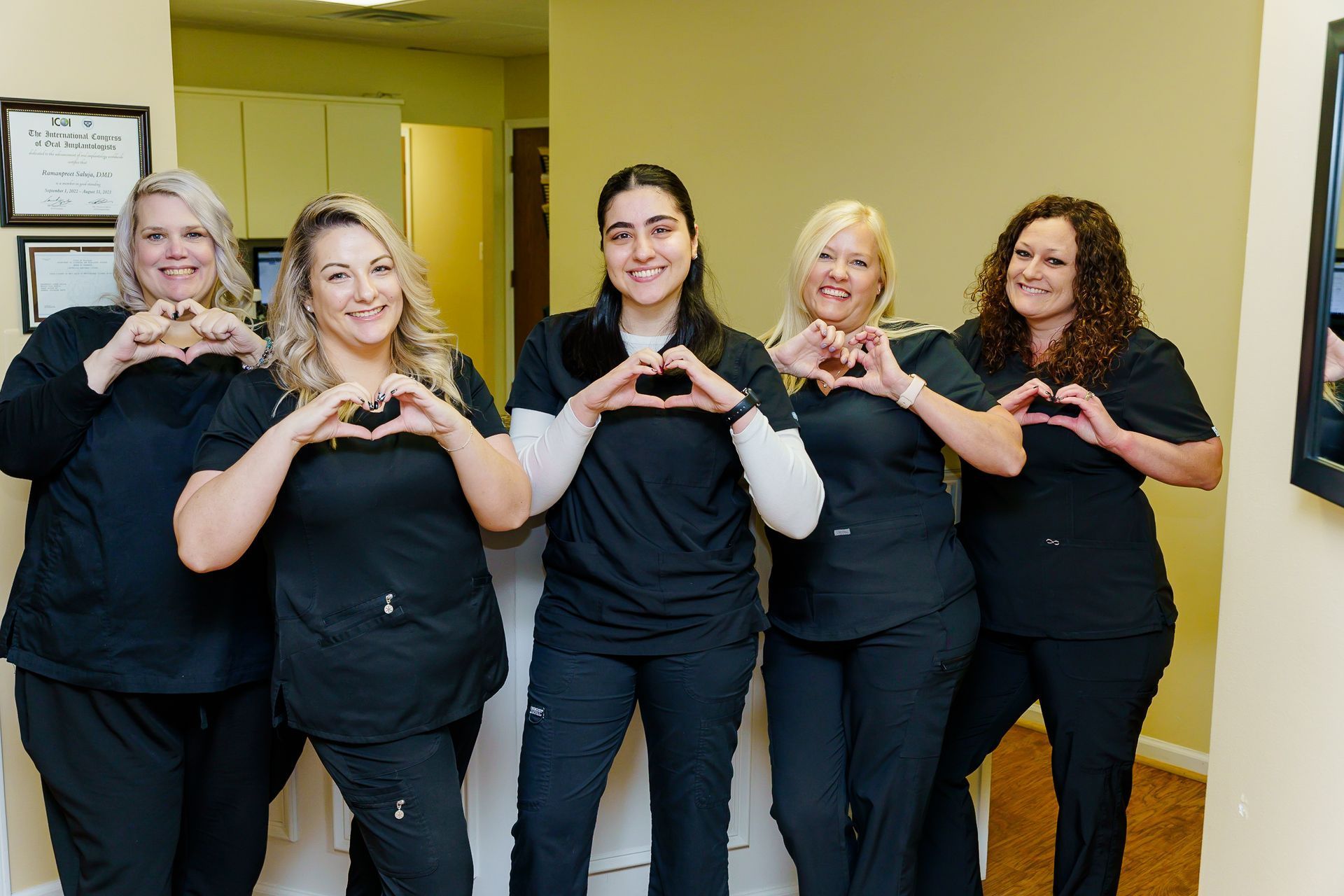 A group of women in scrubs are making a heart shape with their hands.