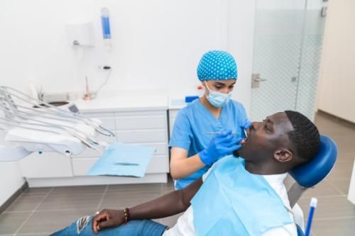 A man is sitting in a dental chair while a dentist examines his teeth.