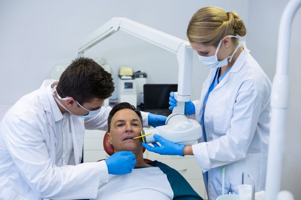 Two dentists are examining a man 's teeth in a dental office.