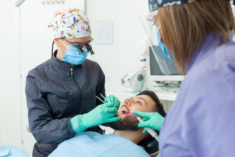 A man is getting his teeth examined by two dentists in a dental office.