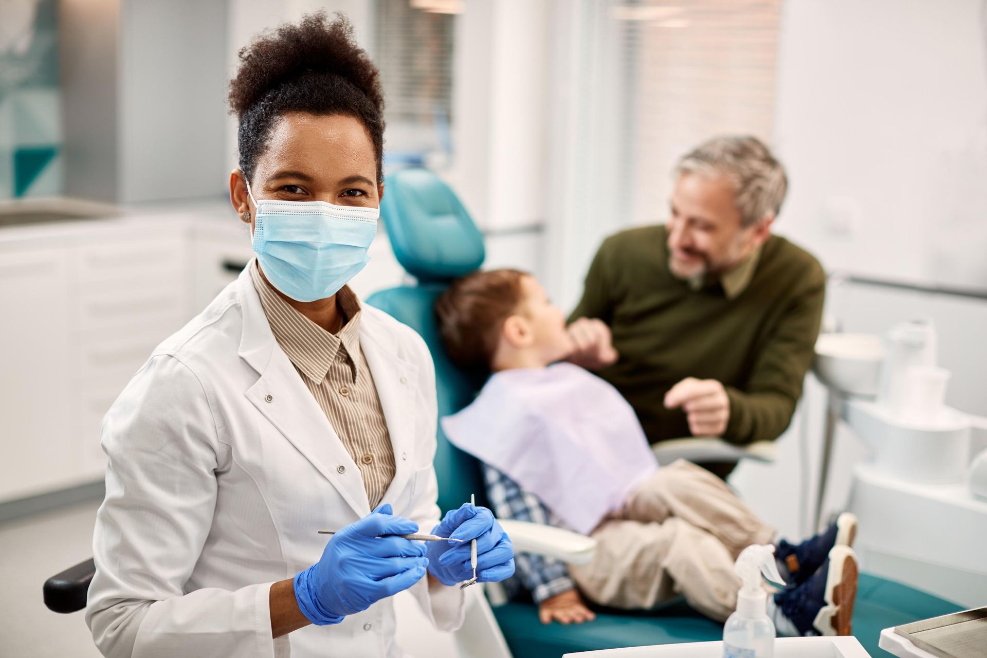 A female dentist is holding a pair of dental instruments in front of a young boy in a dental chair.