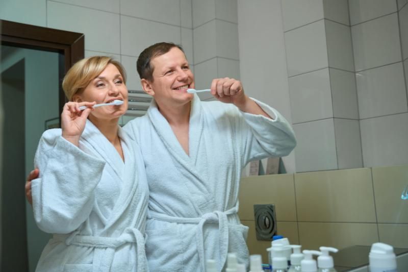 A man and a woman are brushing their teeth in a bathroom.