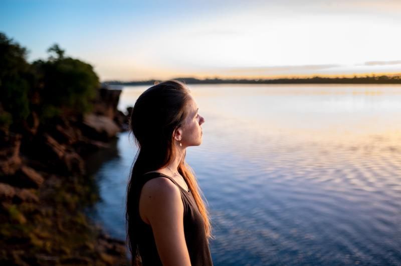 A woman is standing on a cliff overlooking a body of water.