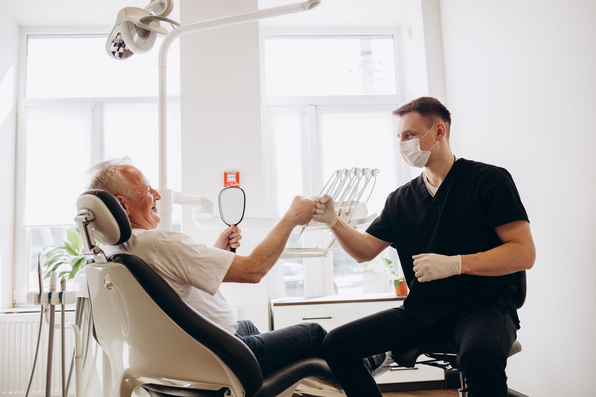 A man is sitting in a dental chair and looking at his teeth in a mirror.