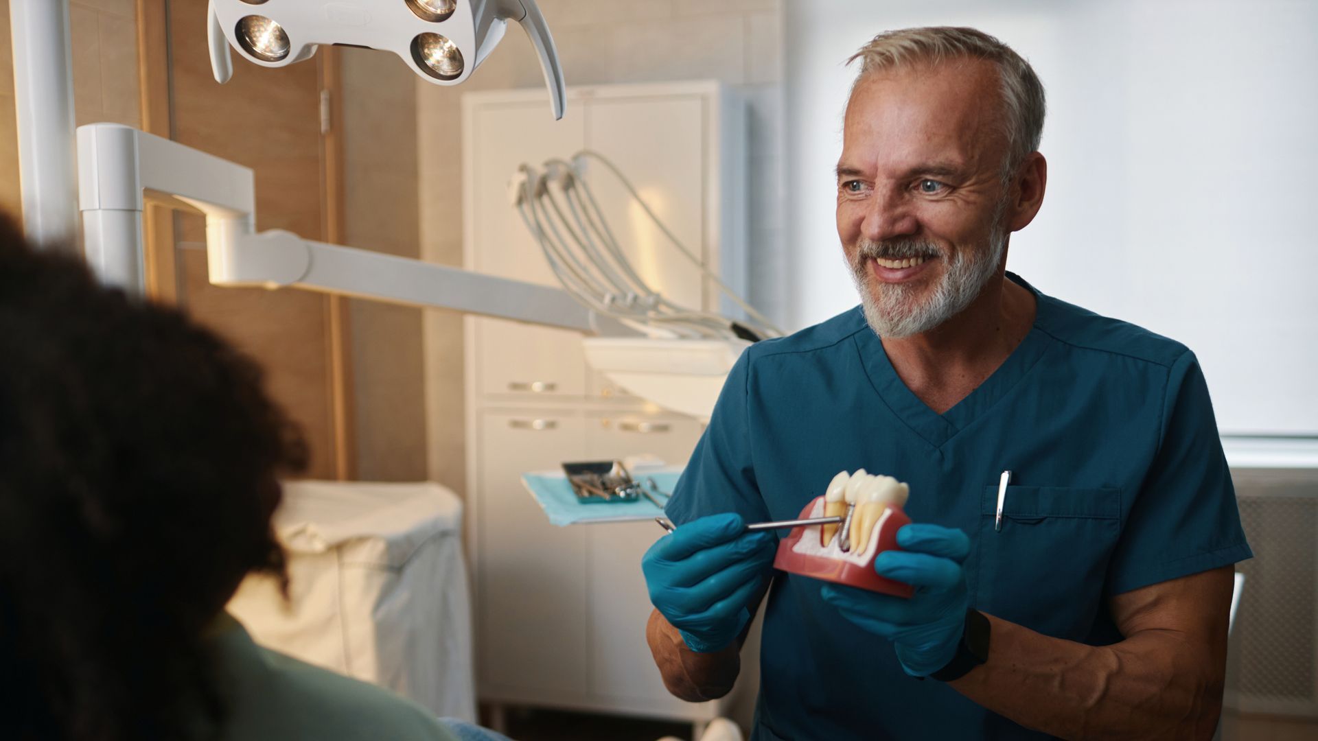 A dentist is holding a model of teeth and smiling while talking to a patient.