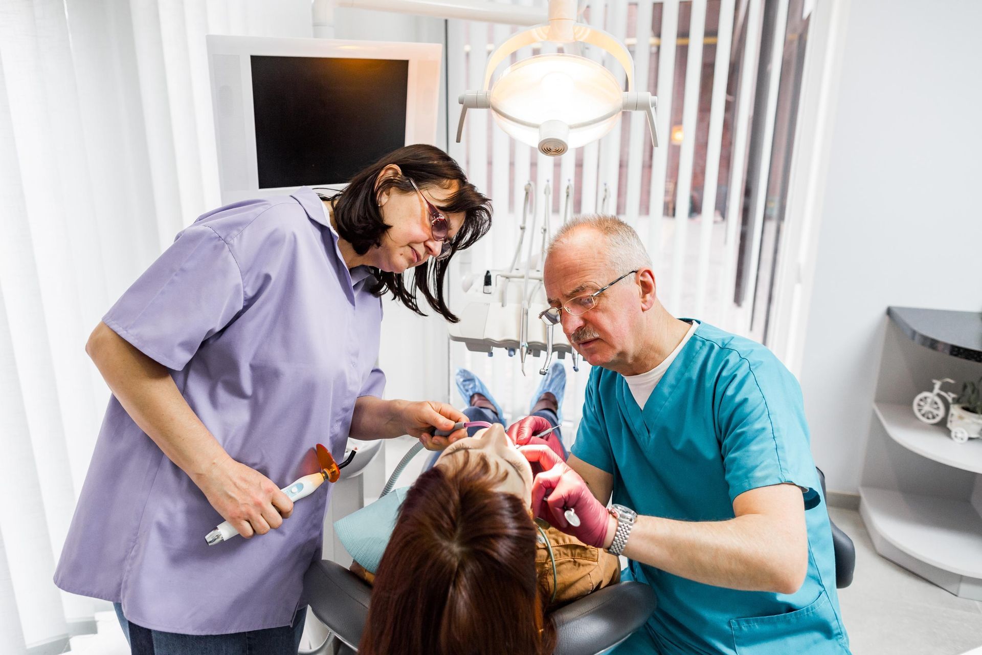 A dentist and a nurse are working on a patient 's teeth in a dental office.