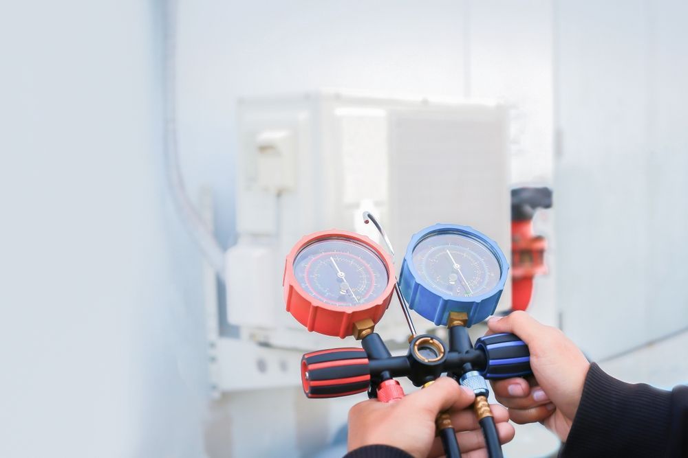 A technician holding a red and blue gauge manifold, checking HVAC unit.