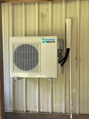 Daikin air conditioner mounted on a corrugated metal wall, with pipes and conduit alongside.
