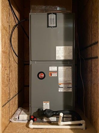 A gray HVAC unit is installed in a wooden enclosure. The unit has labels and pipes at the bottom.
