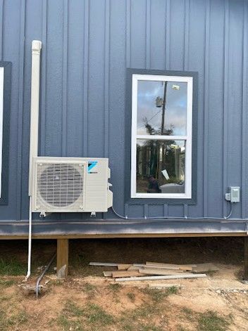 An outdoor Daikin air conditioning unit mounted on a blue building next to a window and a drainpipe.