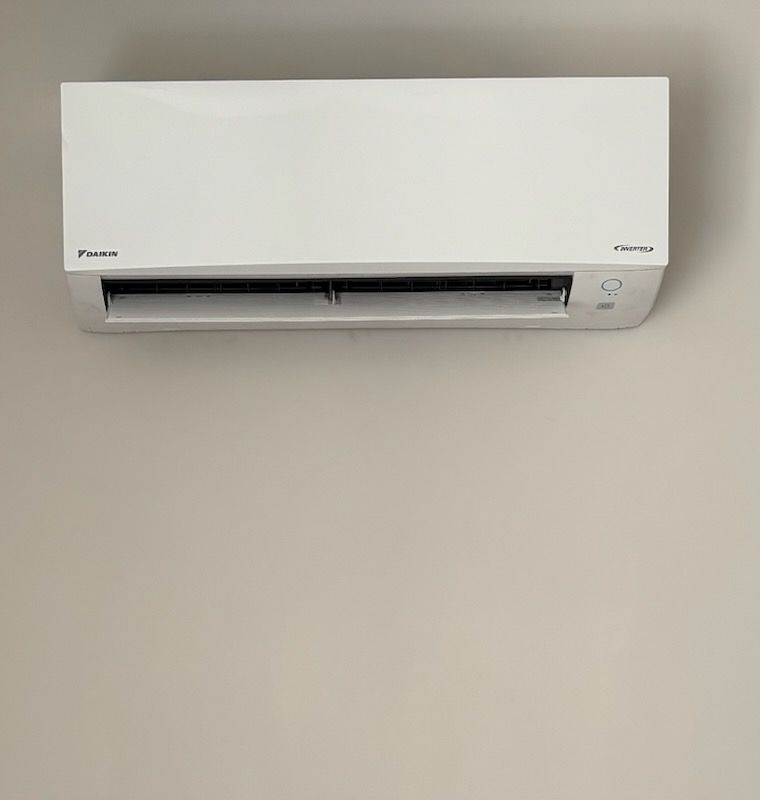 White wall-mounted Daikin air conditioner with black air vents, mounted on a beige wall.