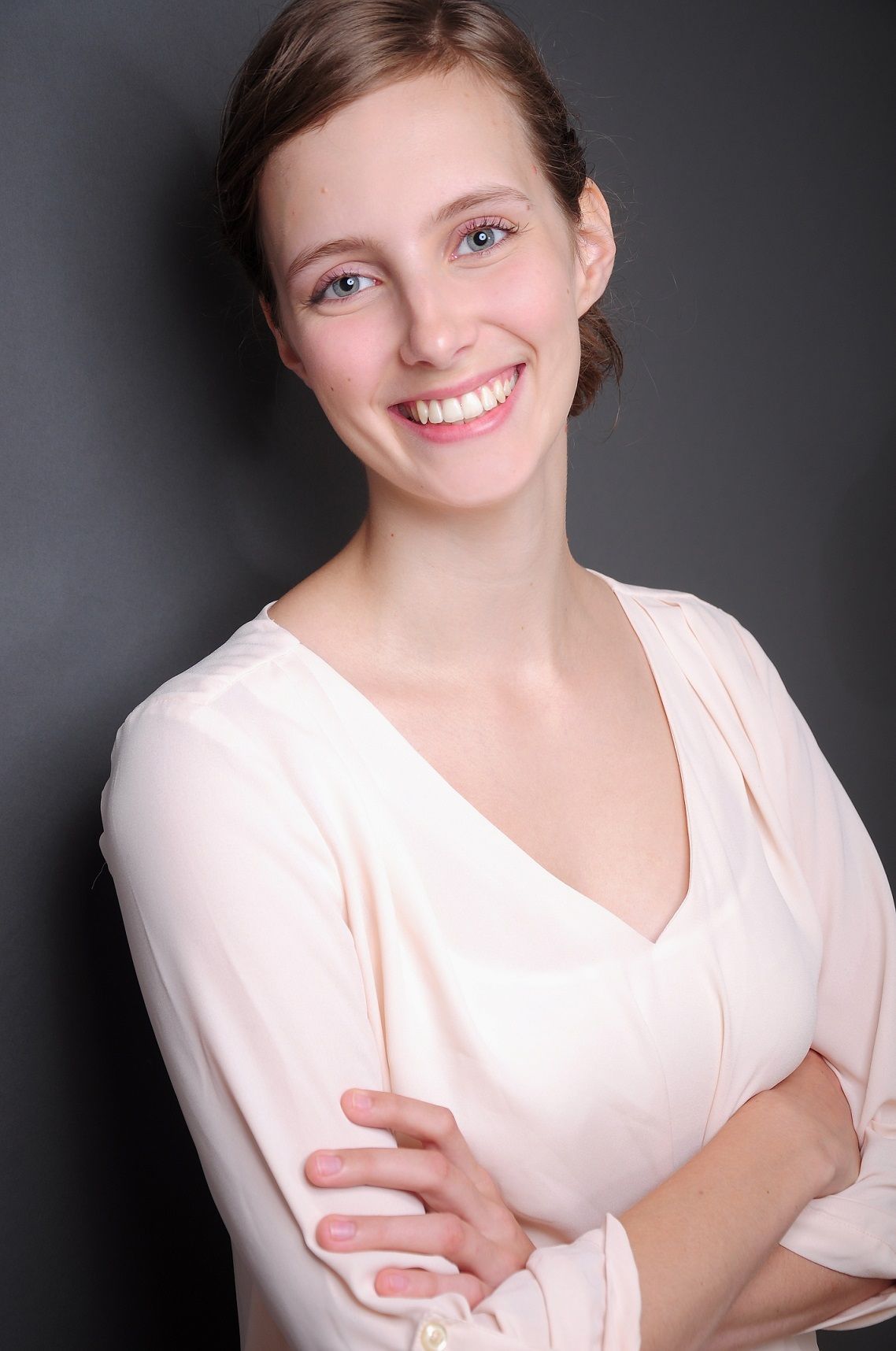 A woman in a white shirt is smiling with her arms crossed.