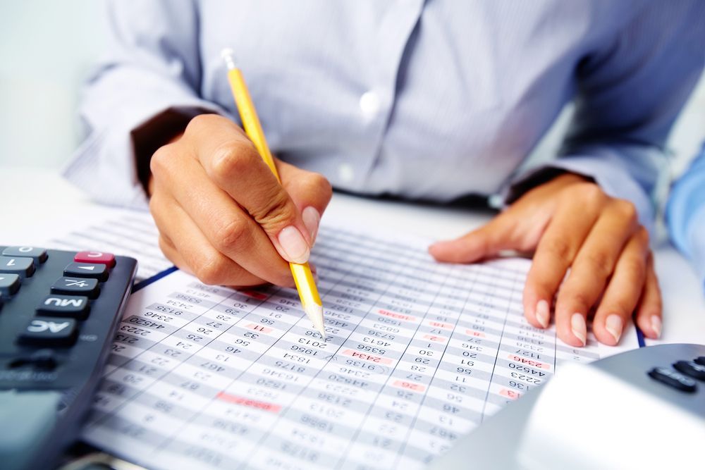 A person is writing on a piece of paper next to a calculator.