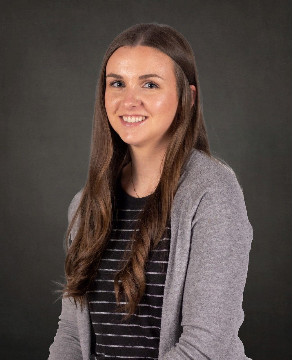 A woman wearing a striped shirt and a gray cardigan is smiling for the camera.