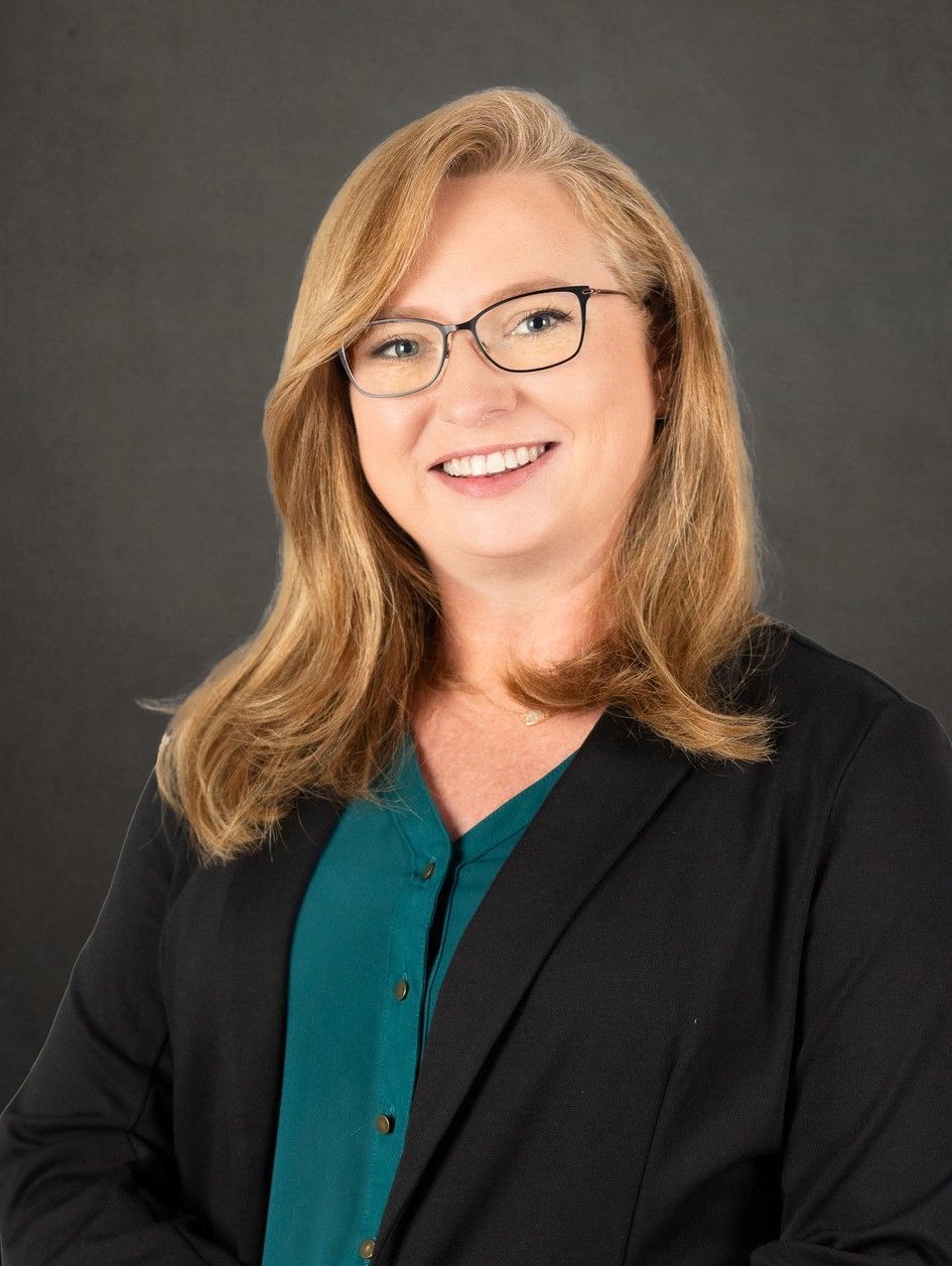 A woman wearing glasses and a black jacket is smiling for the camera.