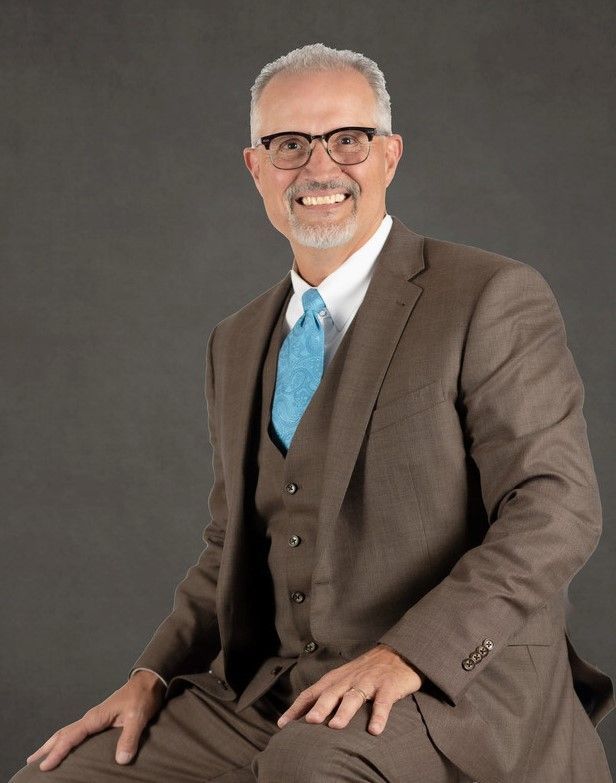 A man in a suit and tie is sitting down and smiling.